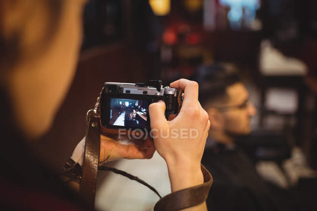 Barbeiro fêmea tirando foto do cliente da câmera digital na barbearia — Fotografia de Stock