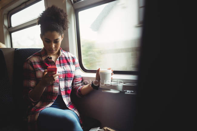 Молодая женщина, сидя в поезде, пользуется мобильным телефоном — стоковое фото