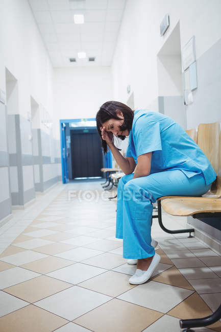 Enfermeira triste sentada em cadeira de madeira no corredor do hospital — Fotografia de Stock