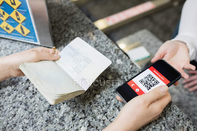 Passager donnant un passeport et un téléphone portable à un préposé à l'enregistrement d'une compagnie aérienne au comptoir d'enregistrement — Photo de stock