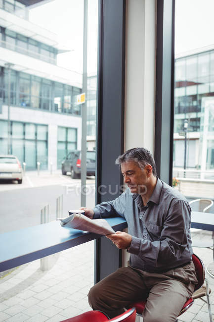 Homem lendo jornal e segurando xícara de café na cafetaria — Fotografia de Stock