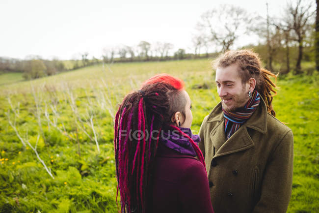 Sonriente pareja cogida de la mano mientras está de pie en el campo de hierba en el parque - foto de stock