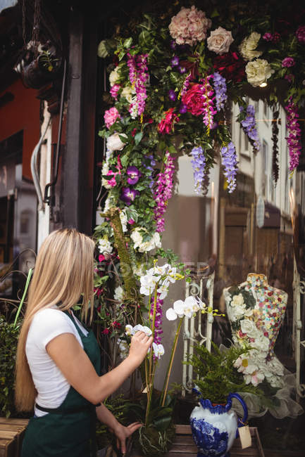 Floristería femenina arreglando flores en jarrón en su tienda de flores - foto de stock