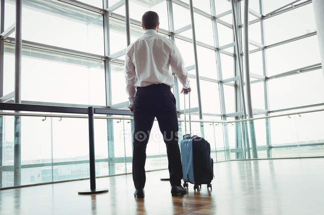 Rückansicht eines Geschäftsmannes mit Gepäck, der durch ein Glasfenster am Flughafen blickt — Stockfoto