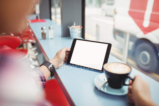 Cropped image of person holding tablet with coffee at restaurant — Stock Photo