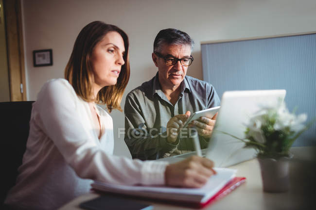 Мужчина и женщина обсуждают за цифровым планшетом и ноутбуком в офисе — стоковое фото