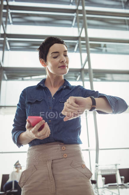 Geschäftsfrau überprüft Uhrzeit bei Handynutzung im Flughafen-Terminal — Stockfoto