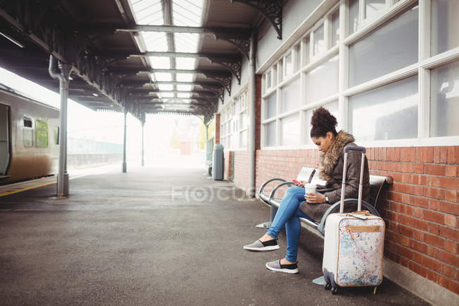 Mujer joven usando el teléfono mientras está sentada en la estación de tren - foto de stock