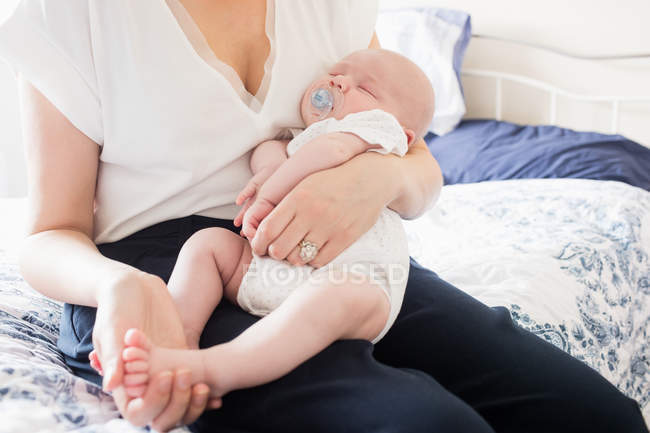 Image recadrée de bébé avec mannequin dormir sur le bras de la mère sur le lit dans la chambre à coucher à la maison — Photo de stock