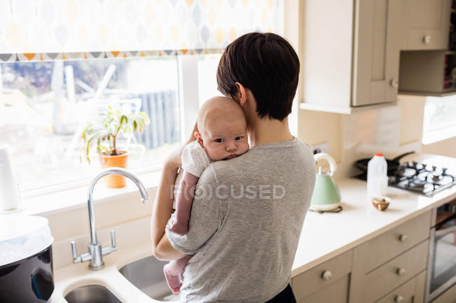 Madre che tiene il suo bambino in cucina a casa — Foto stock