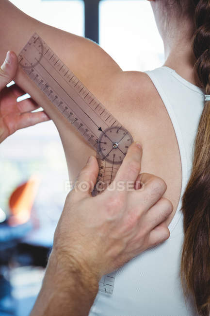 Immagine ritagliata del fisioterapista che esamina la spalla femminile del paziente con goniometro in clinica — Foto stock