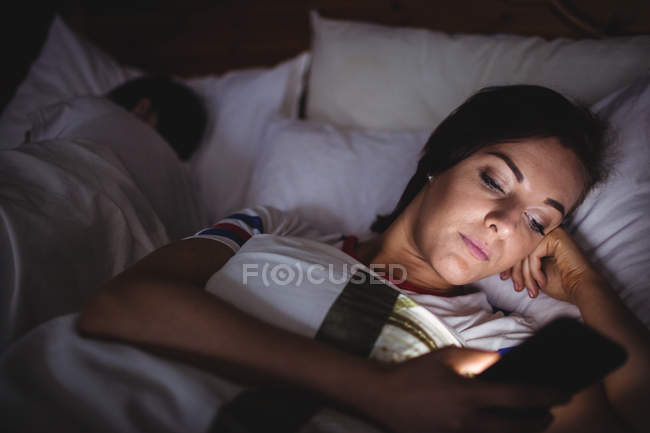Жінка за допомогою мобільного телефону, лежачи на ліжку в спальні — стокове фото