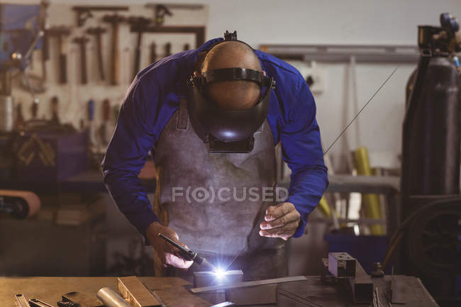 Чоловік зварювальник працює над металом у майстерні — стокове фото