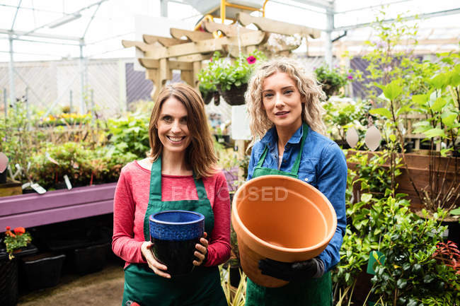 Portrait de fleuristes féminines tenant un pot dans une jardinerie — Photo de stock