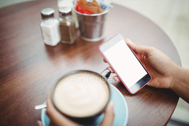 Обрезанное изображение человека, держащего телефон за чашкой кофе в ресторане — стоковое фото