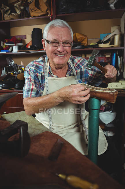 Fröhlicher Schuhmacher hämmert in Werkstatt an einem Schuh — Stockfoto