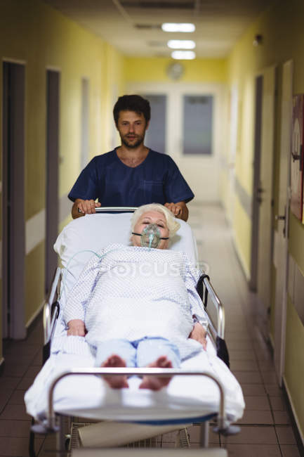 Ward menino empurrando paciente sênior na maca no corredor do hospital — Fotografia de Stock