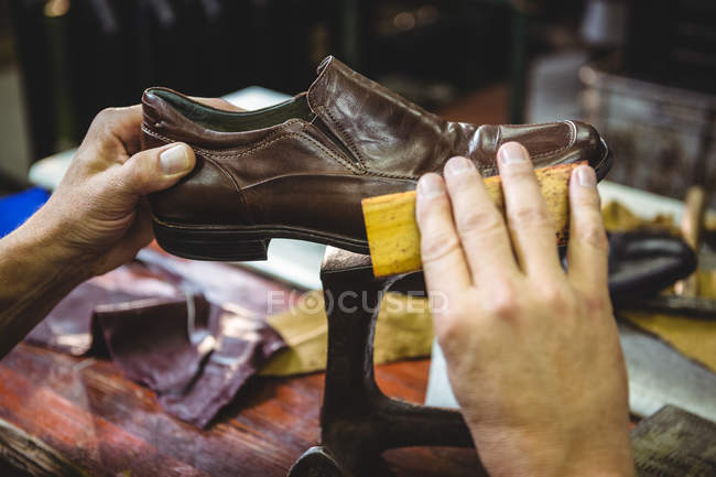 El primer plano del zapatero puliendo el zapato en el taller - foto de stock