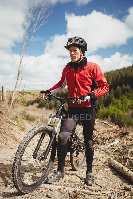 Vista frontal del ciclista con bicicleta en camino de tierra en la montaña contra el cielo - foto de stock