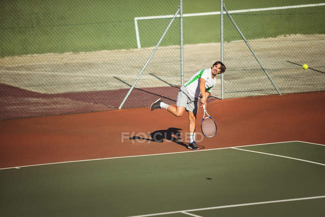 Чоловік грає в теніс в зеленому дворі вдень — стокове фото