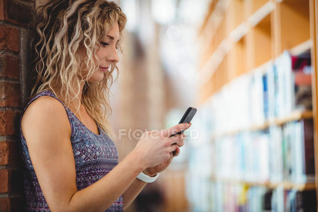 Красива жінка використовує мобільний телефон в бібліотеці — стокове фото