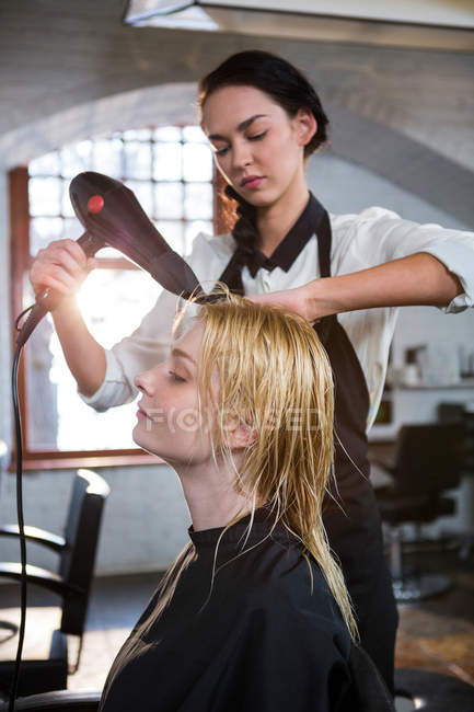 Женщина высушивает волосы феном в парикмахерской — стоковое фото