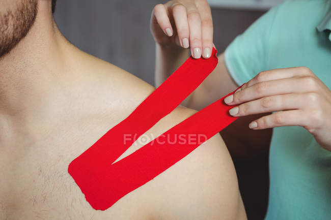 Imagen recortada de terapeuta femenina pegando cinta adhesiva en paciente masculino en la clínica - foto de stock