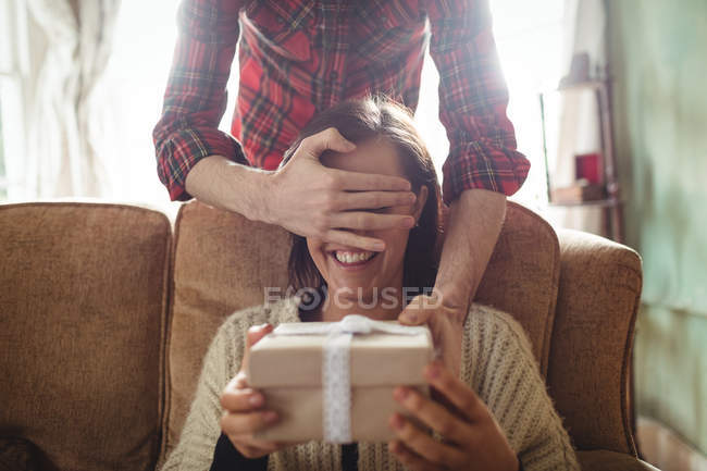 Чоловік дивує жінку подарунком у вітальні вдома — стокове фото