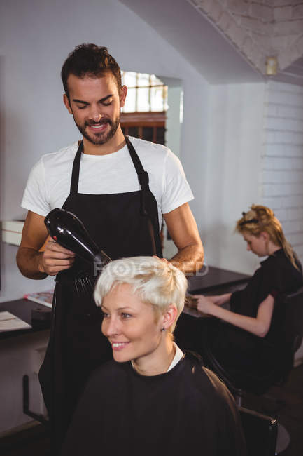 Femme souriante obtenir ses cheveux séchés avec sèche-cheveux au salon de coiffure — Photo de stock