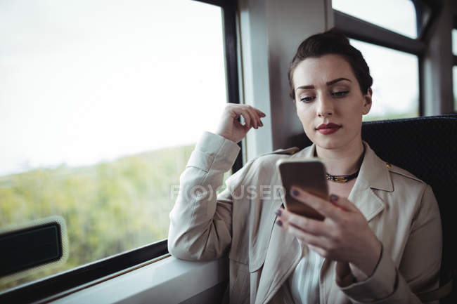 Jovem mulher usando telefone celular enquanto está sentada no trem — Fotografia de Stock