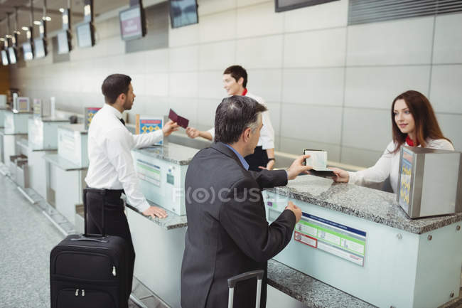 Сотрудники авиакомпании при регистрации вручают паспорт пассажирам на стойке регистрации в аэропорту — стоковое фото