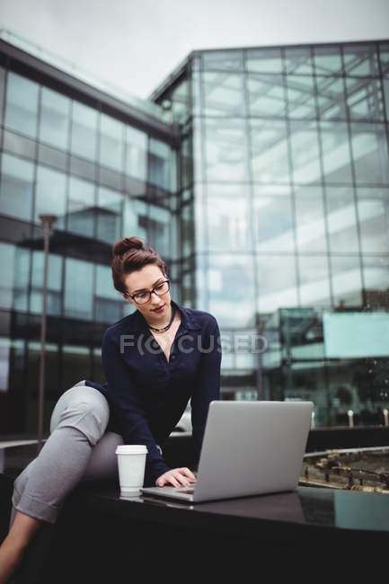 Jeune femme d'affaires utilisant un ordinateur portable contre un immeuble de bureaux moderne — Photo de stock