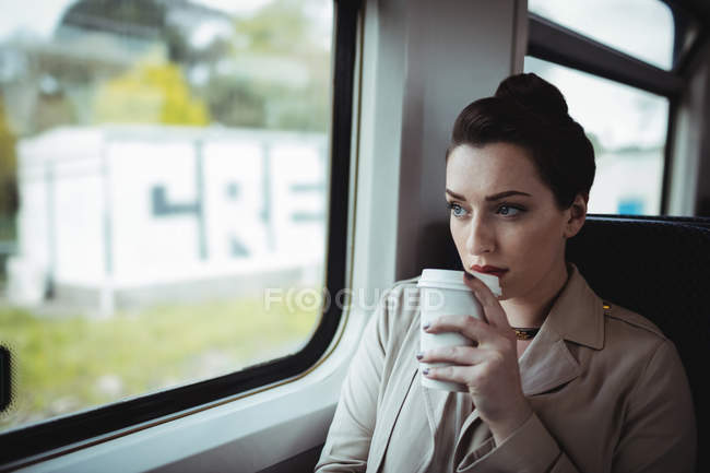 Young woman drinking coffee by window in train — Stock Photo