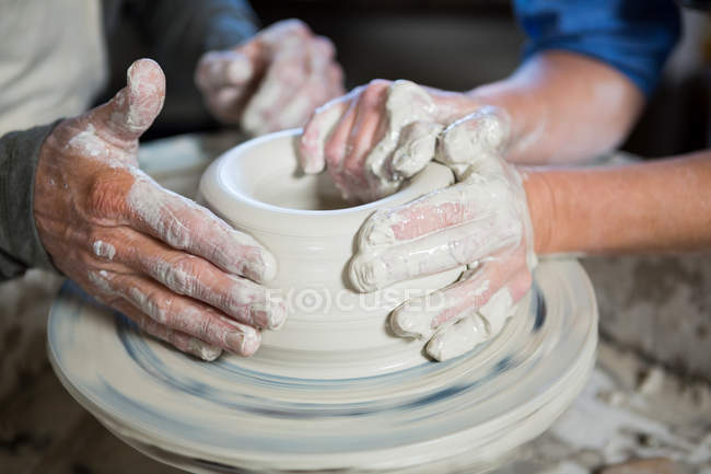 Imagen recortada de alfarero masculino ayudando alfarero femenino en taller de cerámica - foto de stock