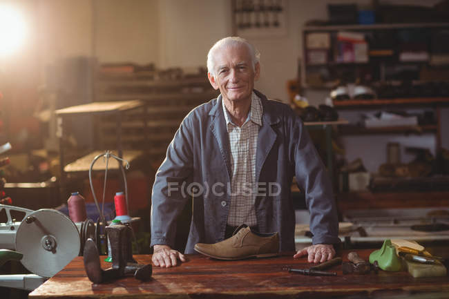 Ältester lächelnder Schuhmacher steht in Werkstatt — Stockfoto