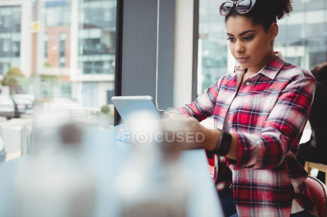 Young woman using digitail tablet while sitting at restaurant — Stock Photo