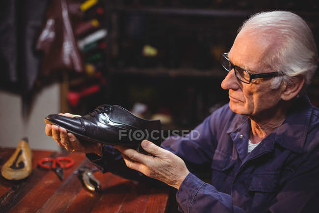 Обувщик осматривает обувь в мастерской — стоковое фото