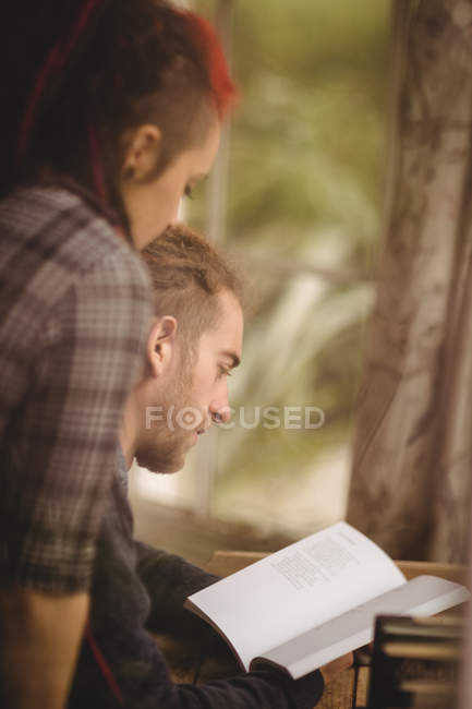 Pareja joven leyendo novela por mesa en casa - foto de stock