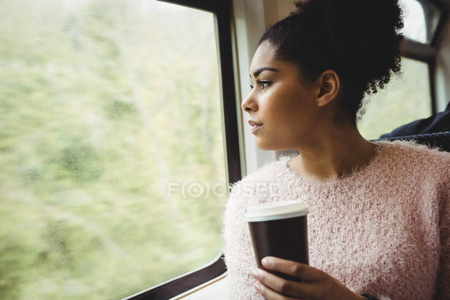 Woman holding disposable coffee cup while sitting in train — Stock Photo