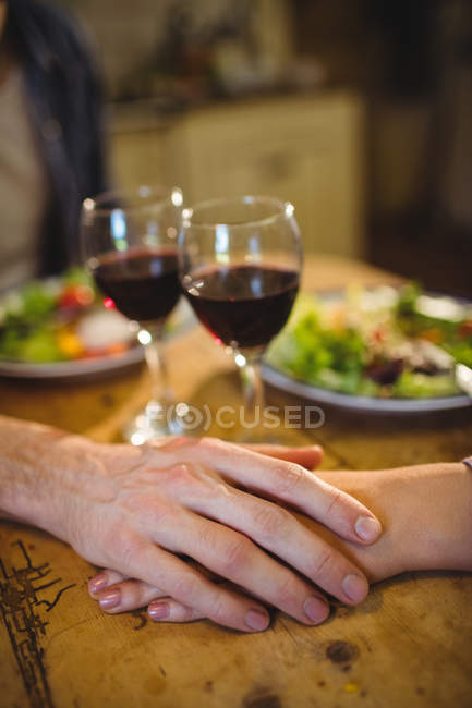 Coppia che si tiene per mano a casa a tavola con bicchieri di vino — Foto stock