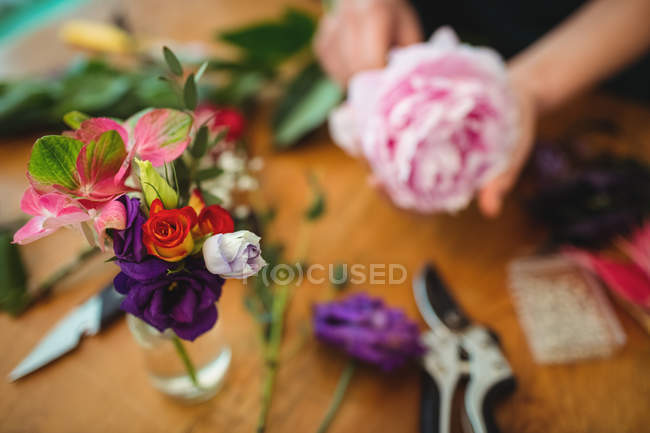 Image recadrée d'un fleuriste tenant une fleur sur le fond, fleurs en bouteille au premier plan — Photo de stock