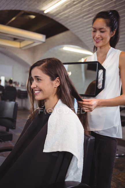 Coiffeuse souriante montrant à la femme sa coupe de cheveux dans le miroir au salon — Photo de stock
