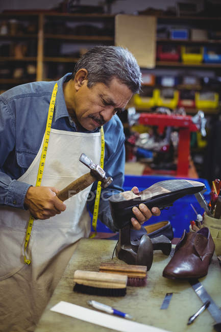 Corrida mista sapateiro sênior martelando em um sapato na oficina — Fotografia de Stock
