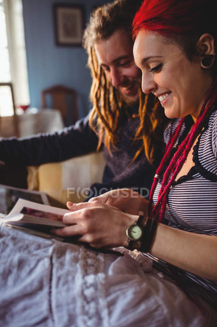Счастливая хипстерская пара ищет фотоальбом, сидя дома — стоковое фото