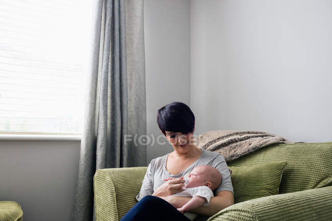 Mãe alimentando seu bebê na sala de estar em casa — Fotografia de Stock