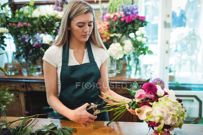 Fêmea florista aparando hastes de flores em sua loja de flores — Fotografia de Stock