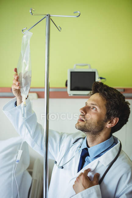 Médico varón revisando un goteo salino en el hospital - foto de stock