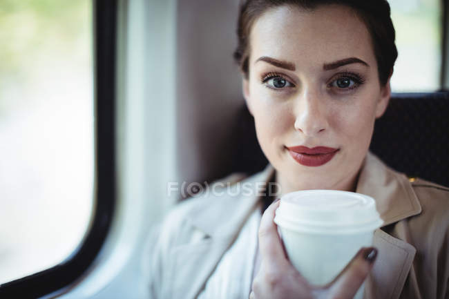 Portrait of young woman holding disposable cup by window in train — Stock Photo