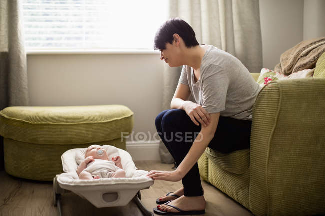 Mutter sitzt auf Sofa und schaut ihr Baby zu Hause im Wohnzimmer an — Stockfoto