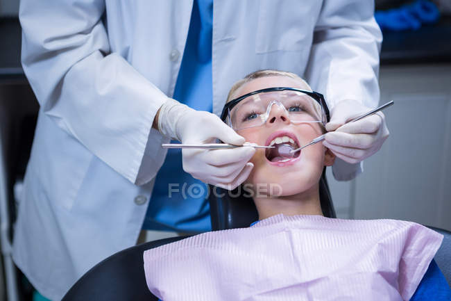 Стоматолог осматривает молодого пациента с помощью инструментов в стоматологической клинике — стоковое фото